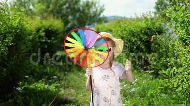 一个小可爱的女孩在温暖的一天在花园里玩一个五颜六色的风车。